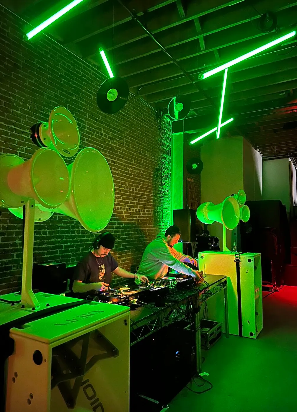 DJs playing through white Void Acoustics speakers under green light