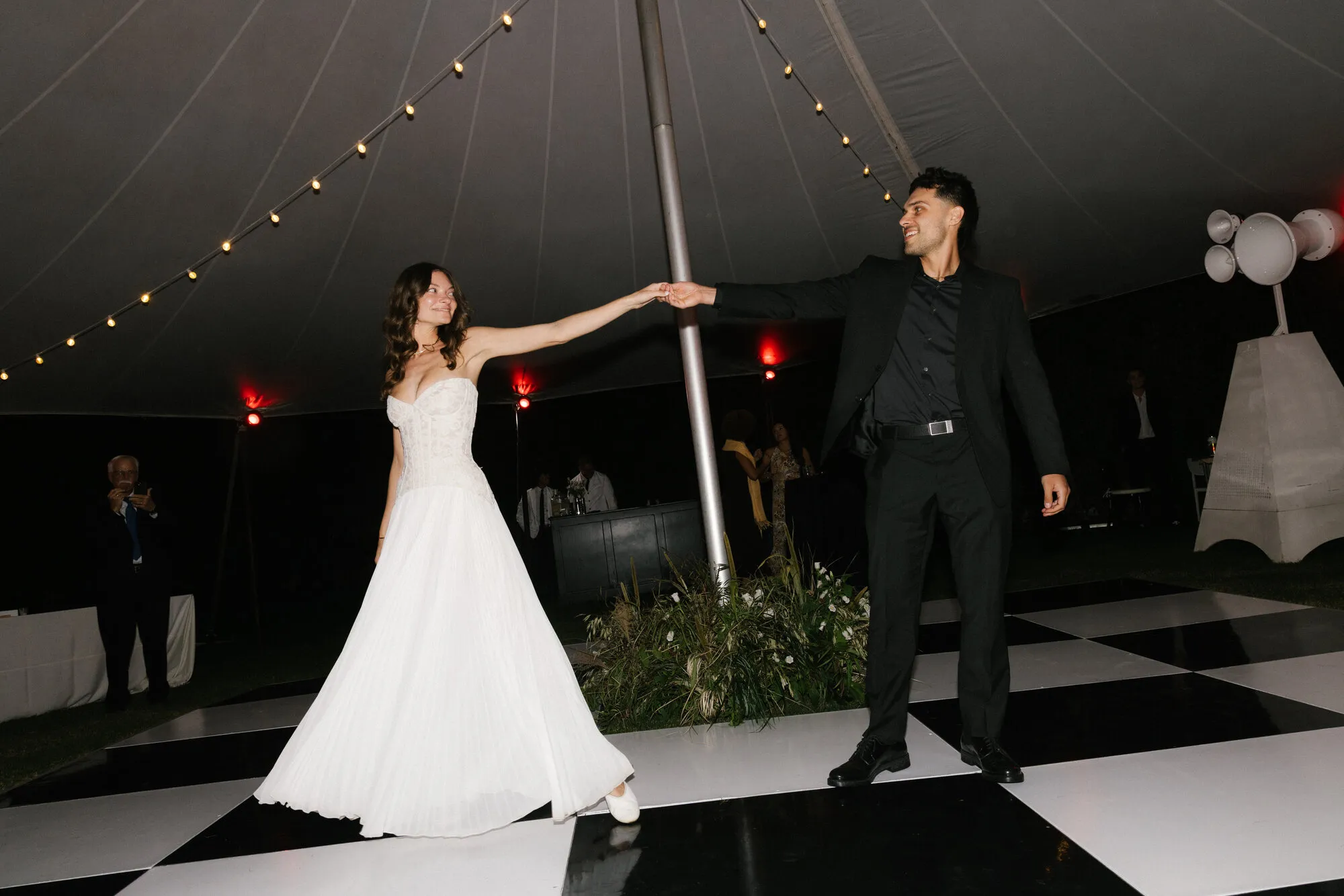 Newlyweds sharing their first dance on a checkerboard floor with white Void Acoustics speakers behind them